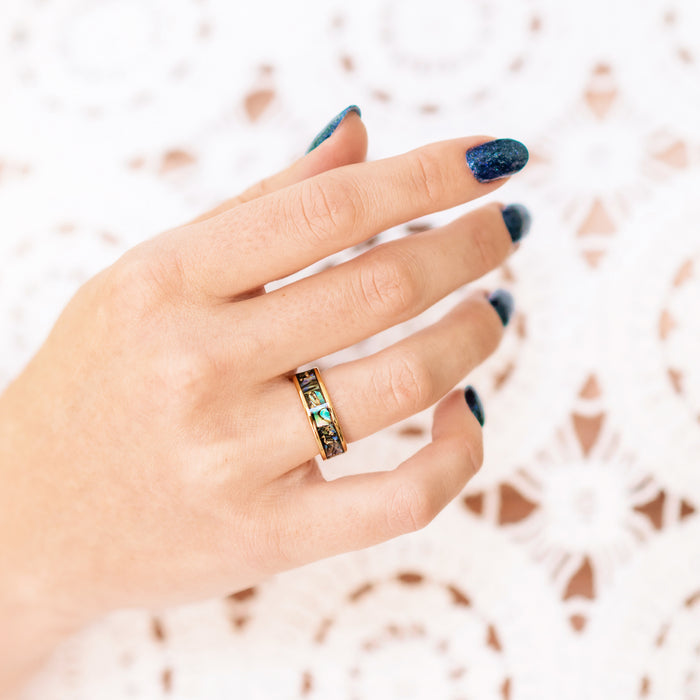 Natural Paula Shell Wedding Band in Yellow Gold Tungsten (6MM) by Aquamarise, shown on hand with dark blue nail polish, featuring a crushed natural Paula shell inlay set in a yellow gold tungsten band, part of Men’s and Women’s Wedding Bands collections.