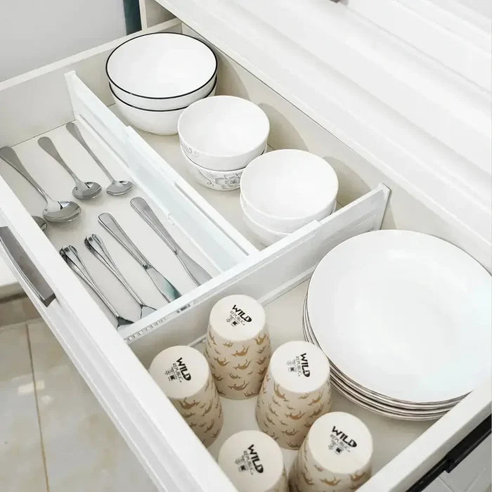 Organized kitchen drawer featuring adjustable drawer dividers, dishes, utensils, and cups.