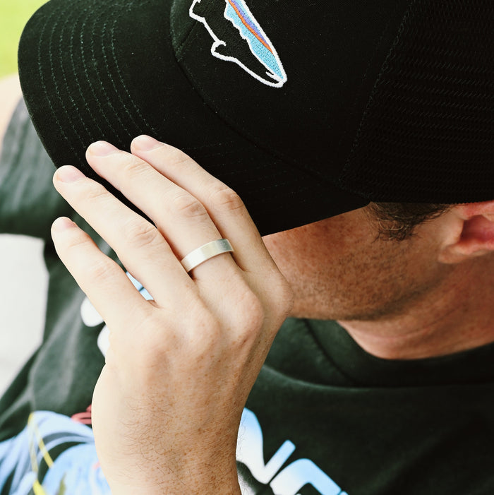 Minimalist Brushed Matte Wedding Band in Sterling Silver (6mm) worn on man's finger, styled casually with black cap, showcasing Aquamarise’s modern men’s sterling silver ring design.