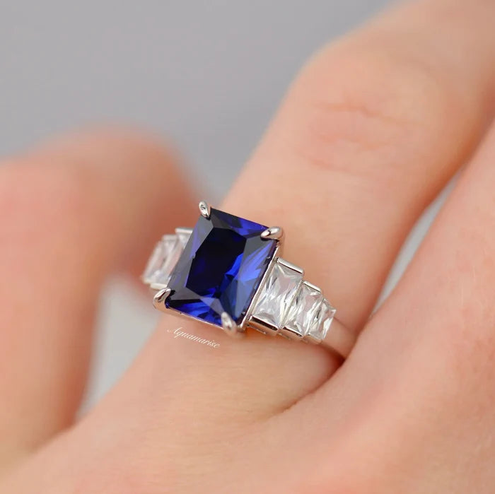 Art Deco Emerald Cut Blue Sapphire Engagement Ring in Sterling Silver featuring a deep blue emerald-cut sapphire center stone flanked by geometric clear baguette accents on a polished band, by Aquamarise, part of Sterling Silver Rings, September Birthstone Jewelry, Engagement Rings for Women, All Jewelry, Birthstone Jewelry, New Arrivals, and Meaningful Jewelry Gifts collections.