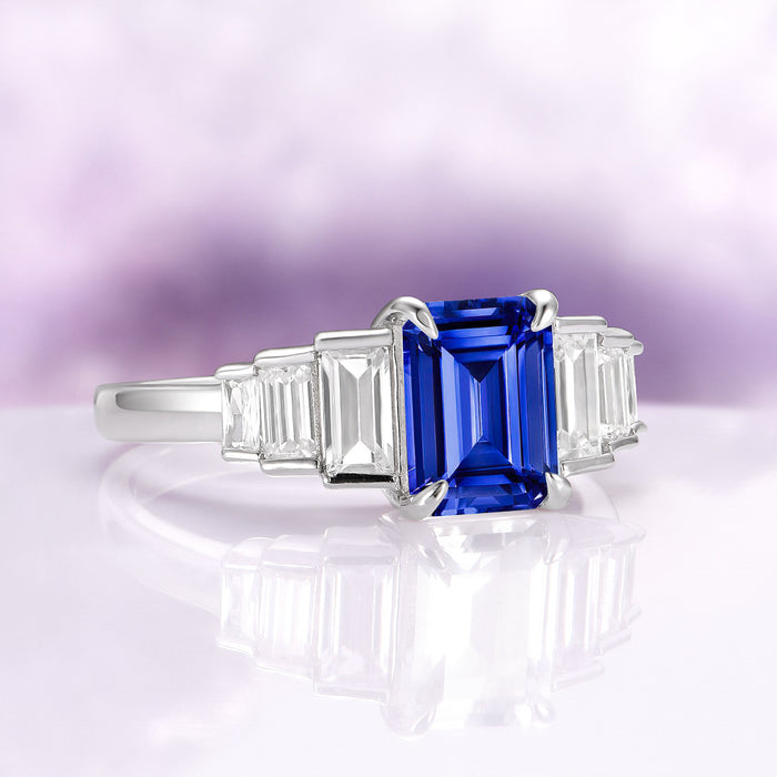 Art Deco Emerald Cut Blue Sapphire Engagement Ring in Sterling Silver by Aquamarise featuring a rich blue emerald-cut sapphire center stone, flanked by geometric baguette clear gemstones on a polished band, ideal for September Birthstone Jewelry and meaningful engagement gifts.