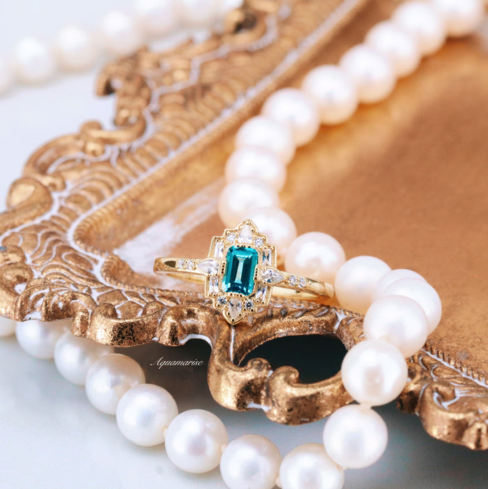 Art Deco London Blue Topaz Engagement Ring in 14K Solid Yellow Gold by Aquamarise Gold with an emerald-cut blue topaz and diamond accents, styled with a classic pearl necklace.