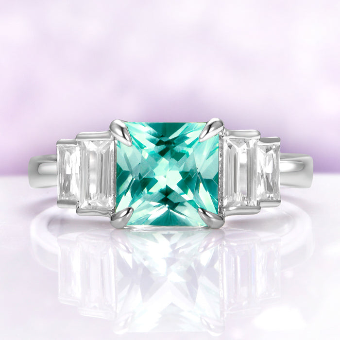 Art Deco Teal Sapphire Engagement Ring in Sterling Silver by Aquamarise, featuring a square teal sapphire center with tapered baguette white gemstones on a polished silver band.