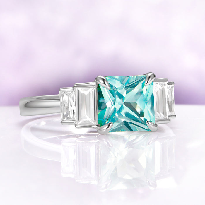 Art Deco Teal Sapphire Engagement Ring in Sterling Silver by Aquamarise, featuring a vibrant teal sapphire center flanked by tapered baguette gemstones on a polished silver band.