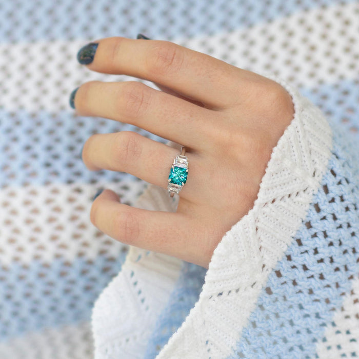 Art Deco Teal Sapphire Engagement Ring in Sterling Silver by Aquamarise, showcasing a vibrant teal sapphire center with baguette accents on a polished silver band.