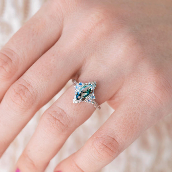 Arwen Moss Agate & Moonstone Ring in 14K White Gold by Aquamarise Gold, featuring a marquise-cut moss agate center stone accented with glowing moonstones on an intricately detailed white gold band, part of nature-inspired and fantasy engagement ring collections.