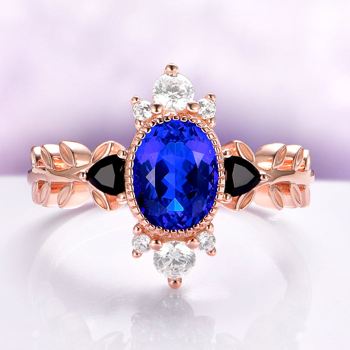 Aurelia Sapphire & Black Onyx Leaf Engagement Ring in 14K Solid Rose Gold by Aquamarise Gold, featuring an oval sapphire, black onyx accents, white gemstones, and a rose gold leaf-inspired band.
