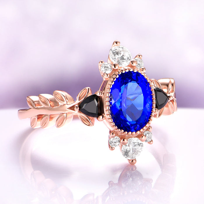 Aurelia Sapphire & Black Onyx Leaf Engagement Ring in 14K Solid Rose Gold by Aquamarise Gold, featuring an oval blue sapphire, black onyx details, and a delicate rose gold leaf-inspired band.