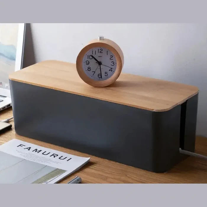 Bamboo cable organizer box on a desk with a clock and notebooks for organized storage of cables and wires.