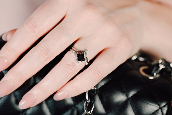 Black Onyx & Meteorite Couples Ring Set by Aquamarise featuring a polished black onyx center stone with diamond accents on a hand resting on a black quilted leather handbag.