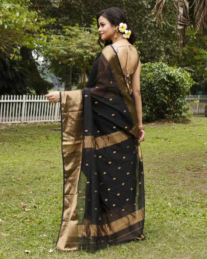Black Maheshwari silk saree with small gold buti across a semi-sheer body and a wide decorative gold border, handwoven in Maheshwar