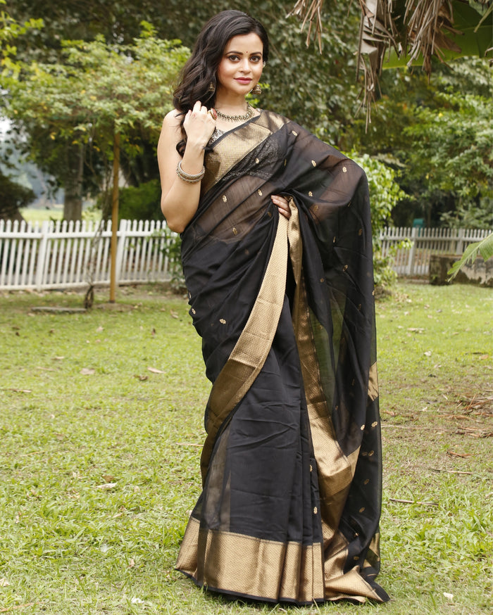 Black Maheshwari silk saree with small gold buti across a semi-sheer body and a wide decorative gold border, handwoven in Maheshwar