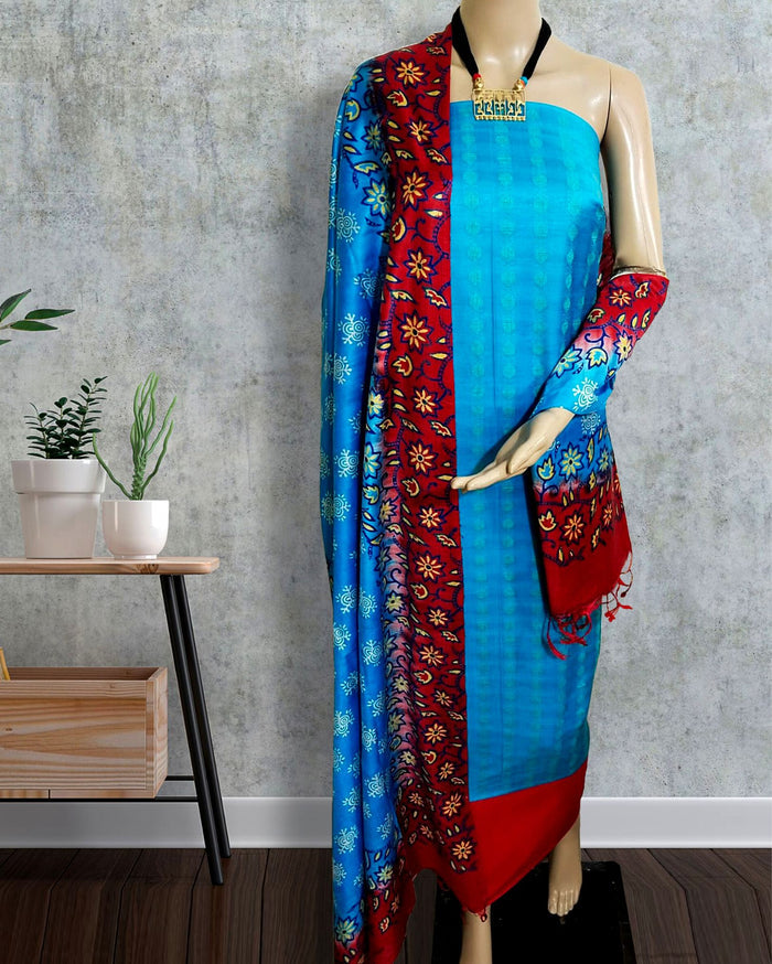 Unstitched blue Katan silk suit set with an asymmetrical split of solid blue and red-edged floral block printed panels, a straight red hem band and a thick vertical printed panel on the dupatta.