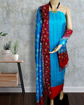 Unstitched blue Katan silk suit set with an asymmetrical split of solid blue and red-edged floral block printed panels, a straight red hem band and a thick vertical printed panel on the dupatta.