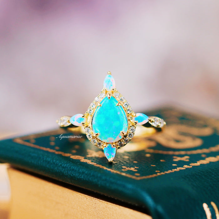 Blue Fire Opal Engagement Ring- 14K Solid Yellow Gold featuring a glowing teardrop blue fire opal surrounded by diamonds, elegantly set by Aquamarise Gold for a magical moment.