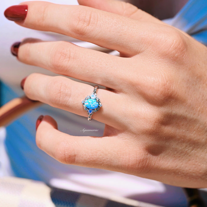 Blue Fire Opal & Opalescent Sapphire Leaf Engagement Ring in Sterling Silver by Aquamarise featuring a glowing blue fire opal center with opalescent sapphires and delicate leaf accents on a hand.