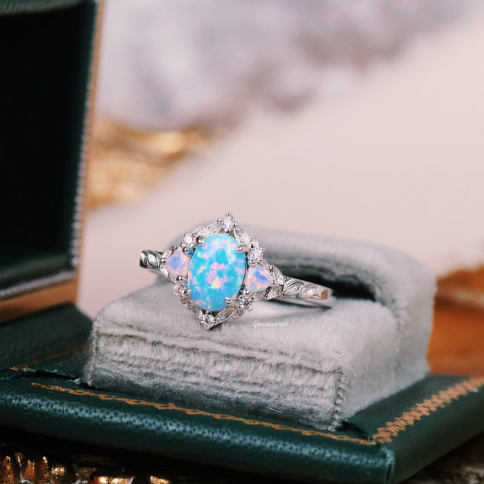 Blue Fire Opal & Opalescent Sapphire Leaf Engagement Ring in Sterling Silver by Aquamarise featuring a glowing oval blue fire opal surrounded by opalescent sapphires on a velvet cushion.