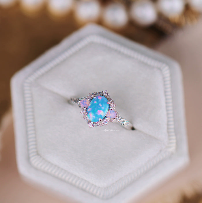 Blue Fire Opal & Opalescent Sapphire Leaf Engagement Ring in Sterling Silver by Aquamarise featuring an oval blue fire opal with surrounding pink and opalescent sapphires on a white velvet cushion.