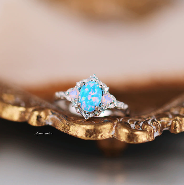 Blue Fire Opal & Opalescent Sapphire Leaf Engagement Ring in Sterling Silver by Aquamarise featuring a vibrant blue fire opal with opalescent sapphires on a decorative gold-toned surface.