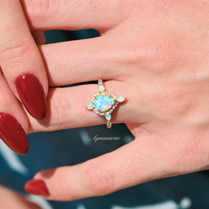 Blue Fire Opal Engagement Ring- 14K Solid Yellow Gold featuring a glowing teardrop opal center with diamond accents, styled elegantly on hand by Aquamarise Gold.