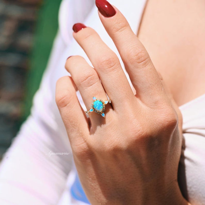 Blue Fire Opal Engagement Ring- 14K Solid Yellow Gold with pear-shaped blue fire opal center and diamond accents, styled on hand by Aquamarise Gold in natural light.
