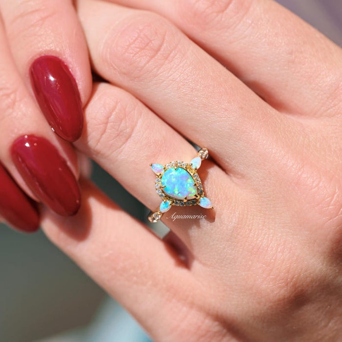 Blue Fire Opal Engagement Ring- 14K Solid Yellow Gold featuring a glowing teardrop opal center with four pear-shaped opal accents, presented by Aquamarise Gold on a hand.