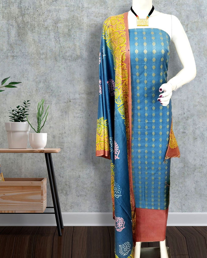 Blue katan silk unstitched suit set with a geometric block-printed tunic, a floral and paisley dupatta in terracotta and mustard, and a broad solid band at the hem.