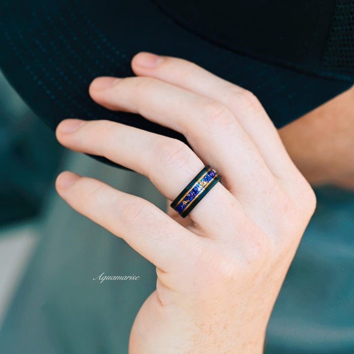Blue Sapphire & Simulated Diamond Gold Leaf Couples Ring Set featuring a black band with blue sapphire and gold leaf inlay, worn on hand, crafted by Aquamarise for matching couples' rings.