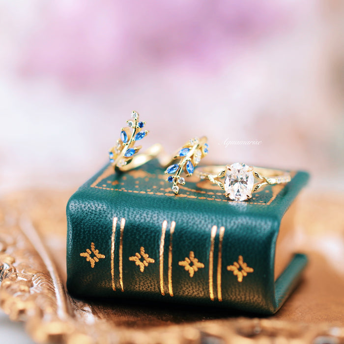 Blue Sapphire & Simulated Diamond Leaf Engagement Ring Set in 14K Yellow Gold Vermeil by Aquamarise, featuring intricate gold leaf designs and sparkling stones on a green leather book display.