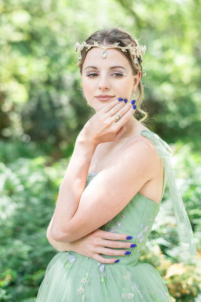 Lab-Grown Diamond & Sapphire Leaf Engagement Ring Set in 14K Solid Yellow Gold (IGI Certified) by Aquamarise Gold, worn on hand with nature-inspired fairy-themed styling and a green floral dress.
