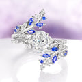 Blue Sapphire & Moissanite Leaf Ring Guard in 14K White Gold by Aquamarise Gold featuring vine and leaf motifs with lab-grown blue sapphires and sparkling moissanite accents.