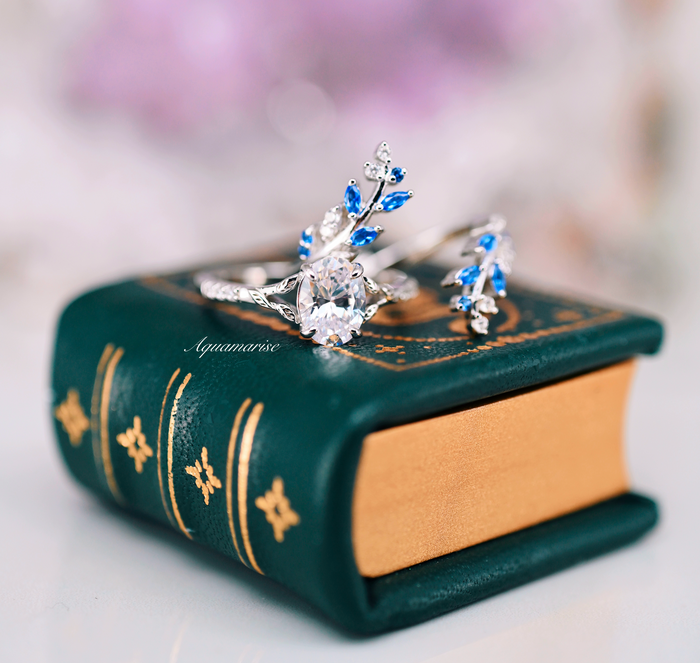 Blue Sapphire & Simulated Diamond Leaf Engagement Ring Set in Sterling Silver featuring delicate blue sapphires and sparkling simulated diamonds displayed on a vintage green leather-bound book.