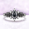Carmilla engagement ring in black ruthenium, oval gray moissanite between black onyx pears with carved leaf and vine shoulders