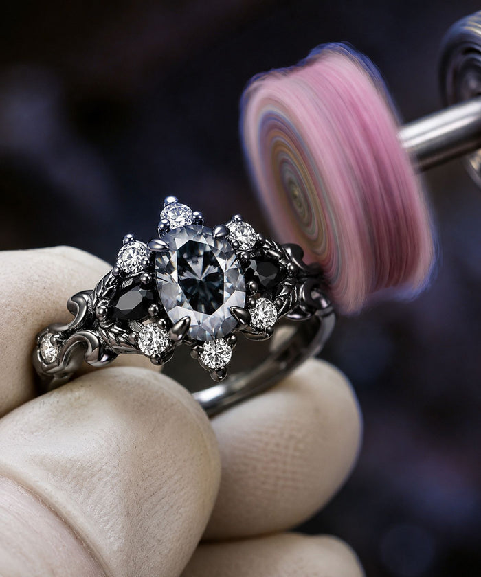 Jeweler polishing a black ruthenium ring set with a grey oval moissanite on a workshop buffing wheel, Aquamarise craftsmanship banner