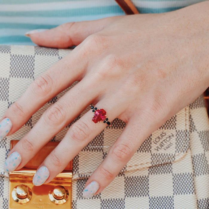 Hand wearing Coffin Cut Ruby and Rose Gold Leaf Couples Ring Set by Aquamarise, featuring a red ruby on a black finish band, styled with a checkered designer handbag.