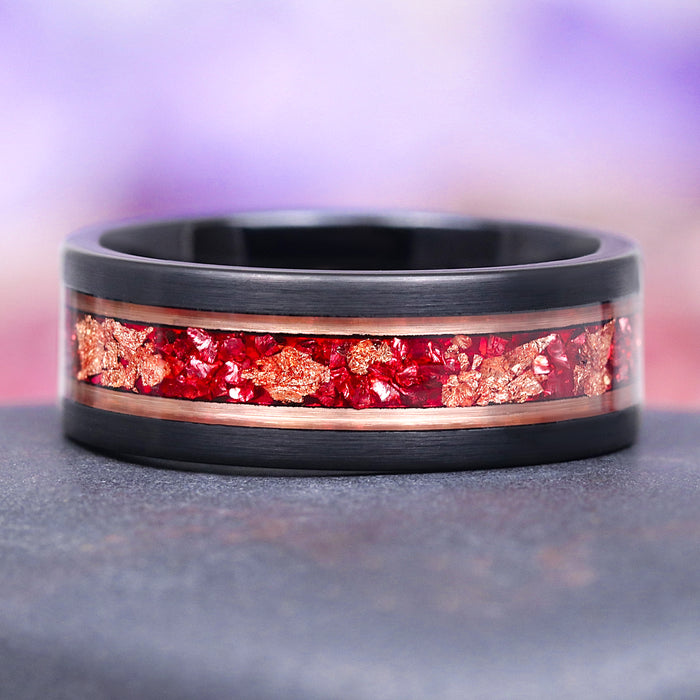 black tungsten carbide men's wedding band with ruby and rose gold inlay on a gray surface with a blurred purple background