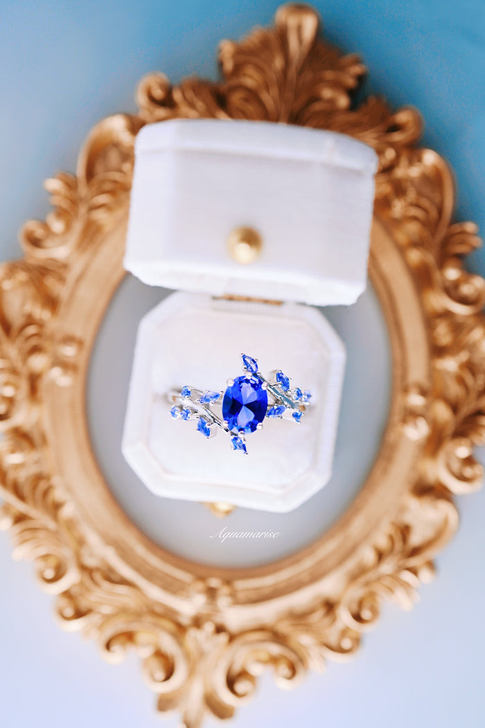Lab-Grown Oval Cut Cornflower Sapphire Leaf Engagement Ring in 14K White Gold by Aquamarise Gold, showcased in a white velvet ring box on an ornate gold frame background.