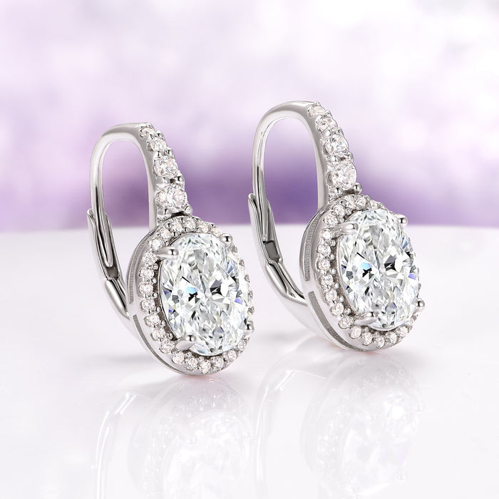 Simulated Diamond Dangle Earrings in Sterling Silver by Aquamarise, showcasing sparkling oval-cut stones surrounded by small accents on a polished drop setting against a soft lavender background.