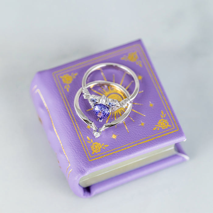 Dawn Court Leather Book Ring Box - Amethyst Light Edition (Small) by Aquamarise with silver rings featuring a purple gemstone on a lavender book-shaped keepsake box.