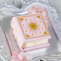 Dawn Court Leather Book Ring Box - Blushing Dawn Edition (Small) by Aquamarise, a soft pink handmade book-shaped ring box with gold celestial design on a silver tray with rose quartz stones.