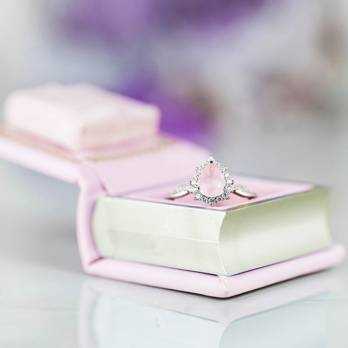 Dawn Court Leather Book Ring Box - Blushing Dawn Edition (Small) by Aquamarise with delicate silver ring featuring a pear-shaped pink stone, displayed on a soft pink leather book-style box.