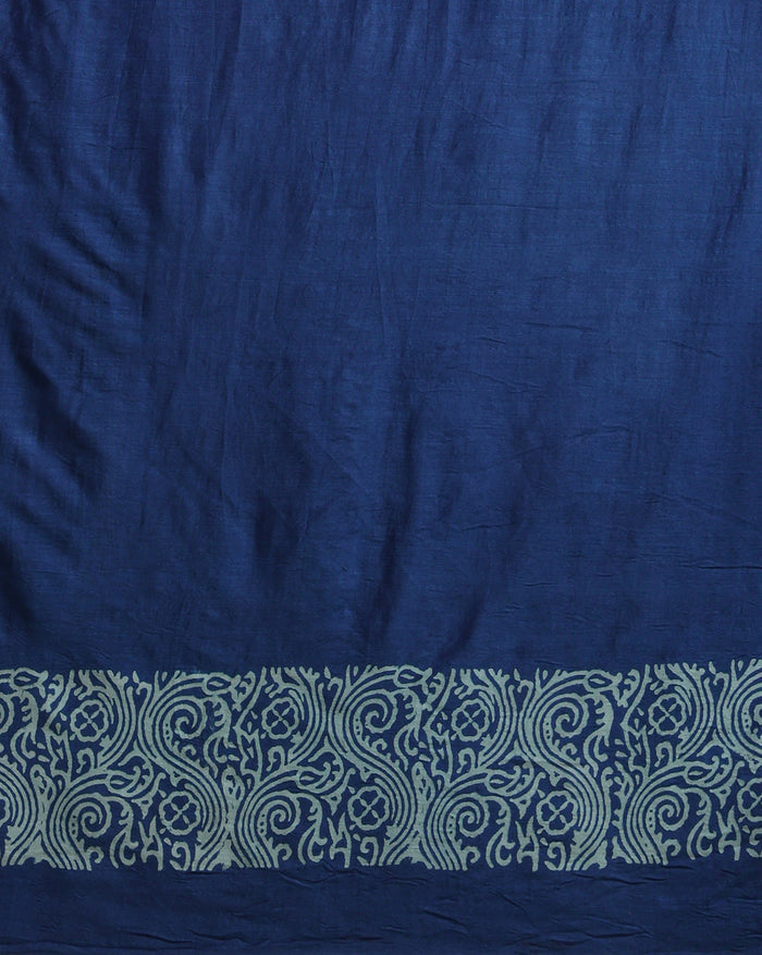 Deep blue katan silk unstitched suit with all-over block-printed floral and diamond motifs, a rust-orange dupatta with wide geometric end borders, and a plain blue bottom.
