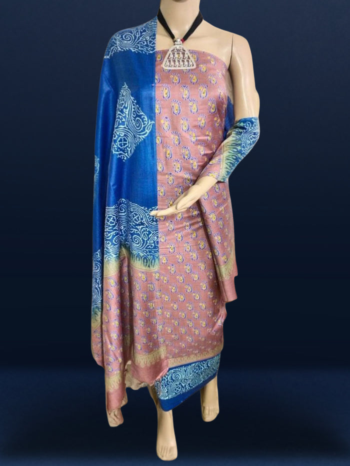 Deep blue katan silk unstitched suit with all-over block-printed floral and diamond motifs, a rust-orange dupatta with wide geometric end borders, and a plain blue bottom.