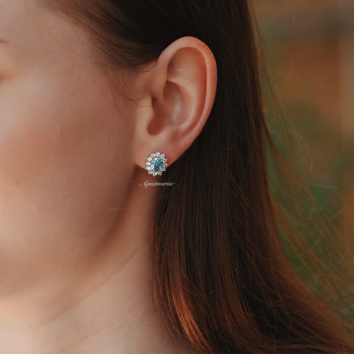 Diana Halo Oval Aquamarine Stud Earrings in Sterling Silver by Aquamarise, featuring oval aquamarine centers surrounded by delicate simulated diamonds on a model's ear.