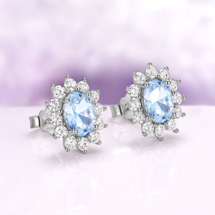 Diana Halo Oval Aquamarine Stud Earrings in Sterling Silver by Aquamarise, featuring sparkling oval aquamarines surrounded by radiant simulated diamonds on a soft purple background.