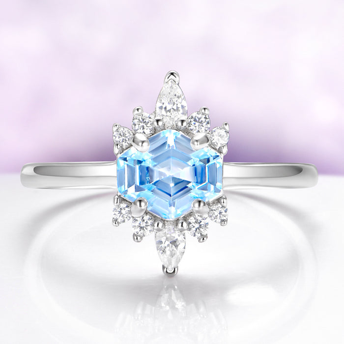 Silver ring with a blue gemstone and diamond accents on a light purple background
