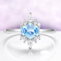 Silver ring with a blue gemstone and diamond accents on a light purple background