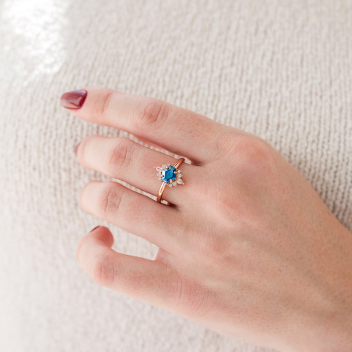 Hand wearing a ring with a blue gemstone on a textured white background