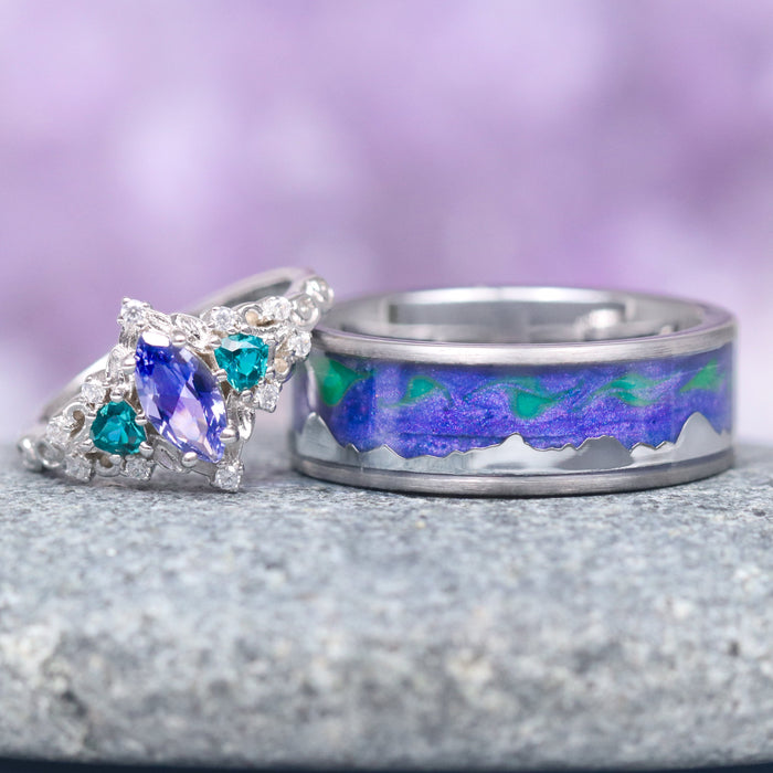 Borealis Tanzanite & Teal Sapphire Couples Ring Set (Mountain Range) by Aquamarise features a marquise-cut tanzanite with teal sapphire accents and a silver band with an iridescent mountain range design, from Matching Couples' Rings and September and December Birthstone Jewelry collections.