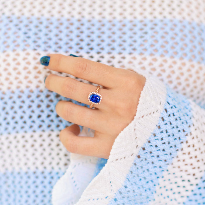 Blue Sapphire Engagement Ring Cushion Cut Ceylon Sapphire on hand over textured blue and white background
